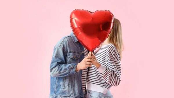 Casal se beijando atrás de balão em forma de coração em um fundo rosa.