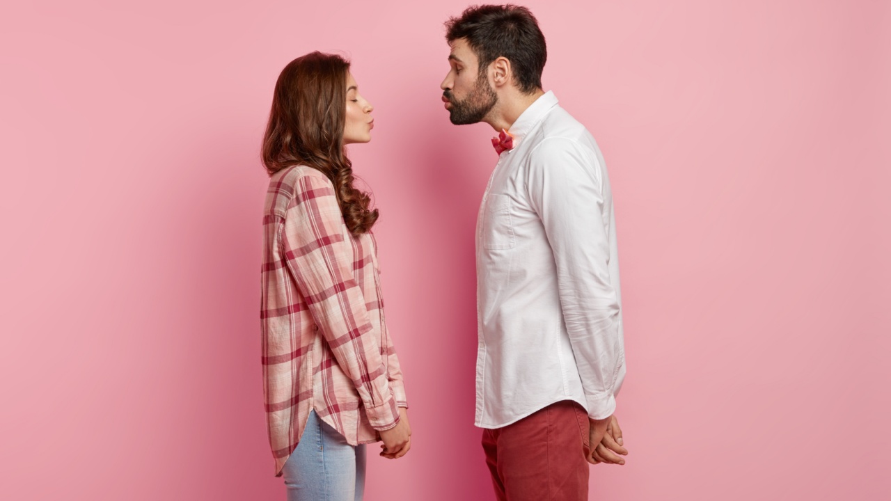 casal fazendo bico para se beijar mas afastado em fundo rosa