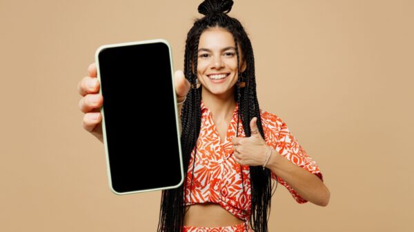 mulher negra com tranças no cabelo apontando um celular para a lente da câmera em fundo marrom claro