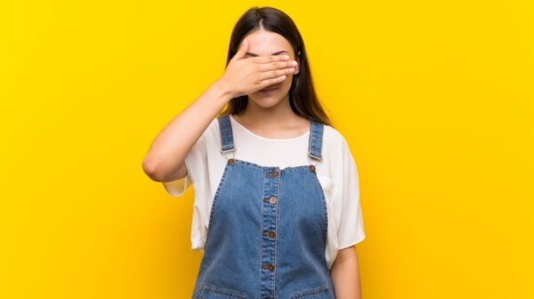 mulher com a mão esquerda tampando os olhos em fundo amarelo