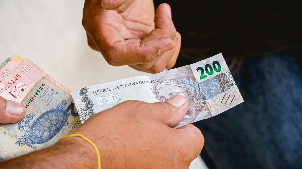 mão masculina entregando uma nota de duzentos reais para outra mão masculina