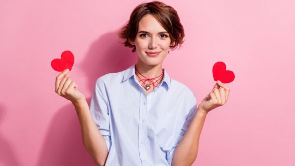 mulher com camisa branca segurando dois corações vermelho de papel, um em cada mão, em fundo rosa