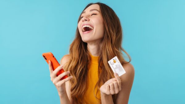 mulher segurando um cartão na mão esquerda e o celular na mão direita e gargalhando em fundo azul