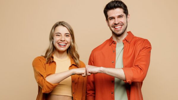 casal sorrindo para a camera e dando um soquinho em fundo marrom