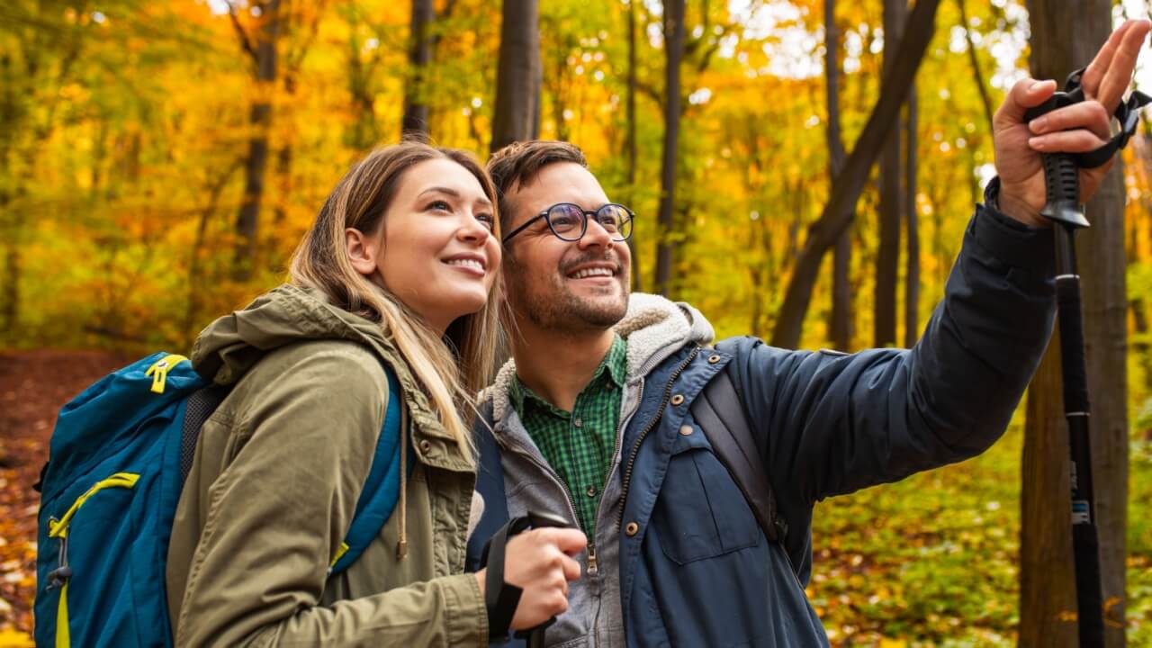 casal carregando mochilas em uma paisagem de outono